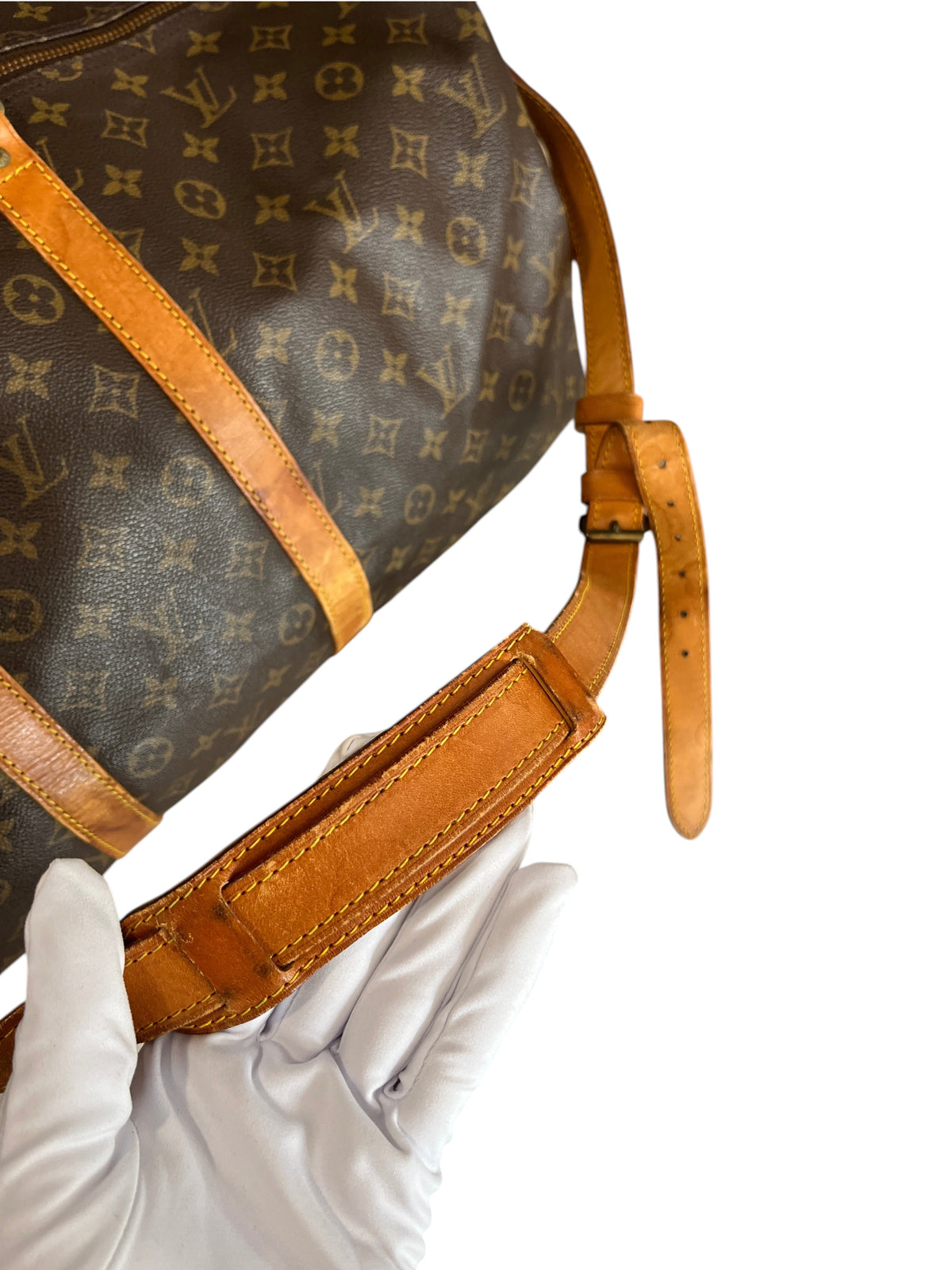 Détail de la bandoulière en cuir patiné du sac de voyage Louis Vuitton Keepall 55 vintage chez vinqo.store