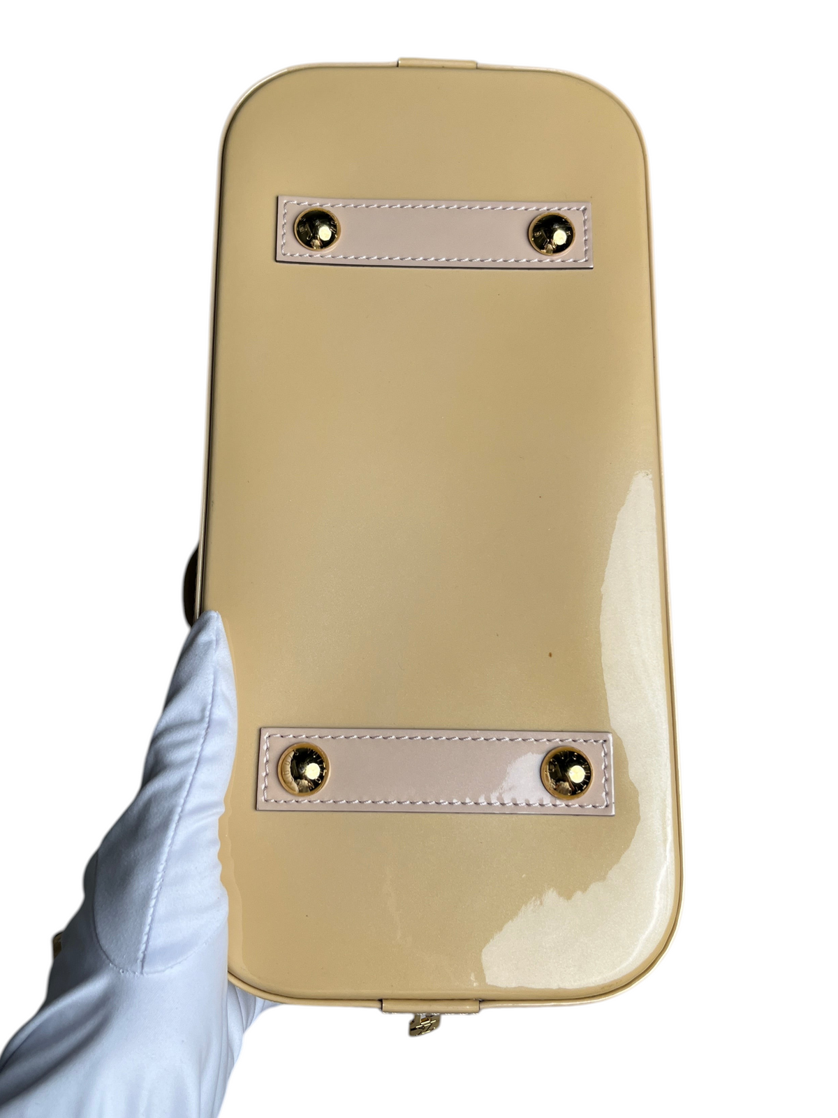 Vue de dessous du sac Louis Vuitton Alma PM Verni beige avec finitions en cuir verni et clous dorés chez vinqo.store