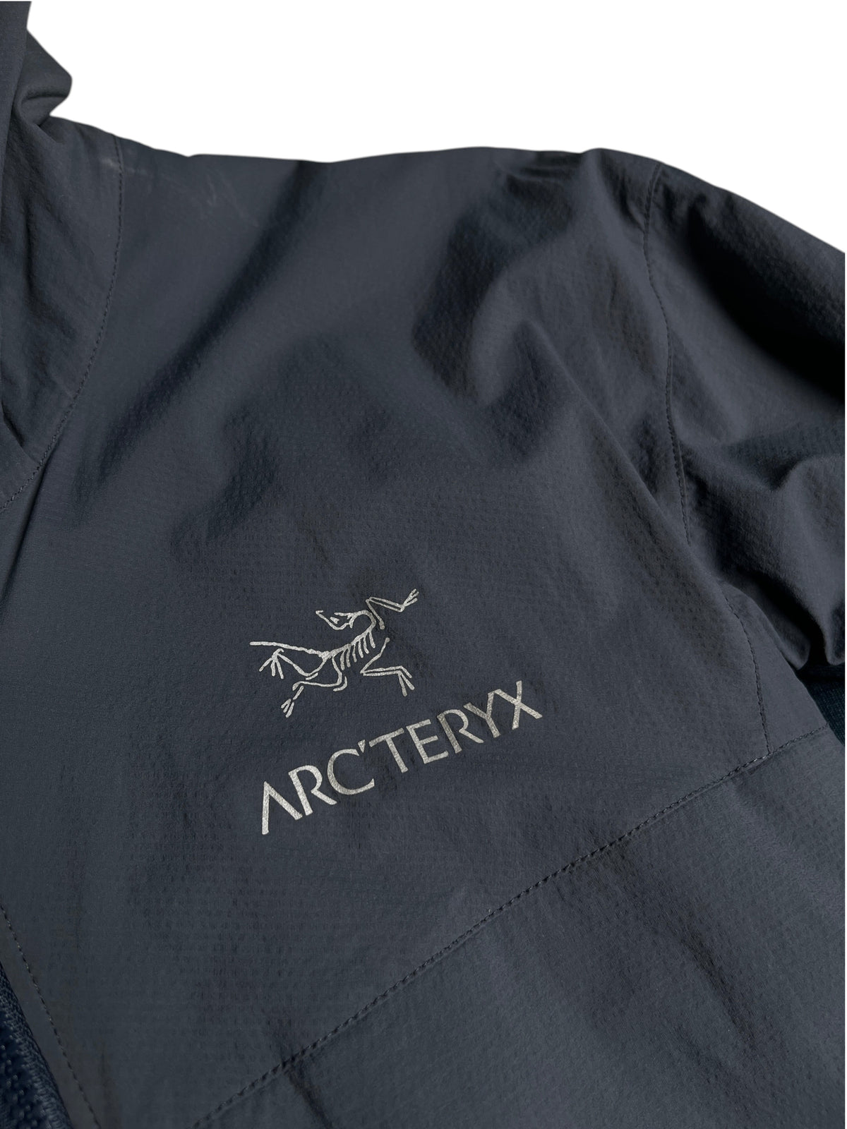 Logo brodé Arc'teryx sur une veste technique bleu marine de vinqo.store